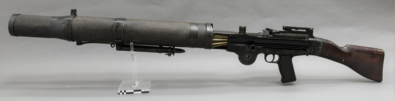 Left side of an American Lewis machine gun. The barrel is a large diameter tube with fins at the rear. Brown wood pistol grip and buttstock. 