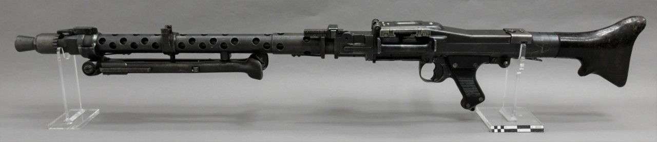 Left side view of a German MG34 machine gun. Metal gun with dark patina, black plastic pistol grip and black plastic buttstock. 