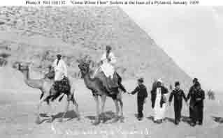 Sailors (wearing Fez hats) accompanied by local guides on camels at base of one of the Giza Pyramids during Egyptian sightseeing tour, January 1909.
