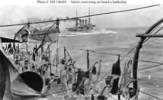 Sailors perform calisthenics on a battleship's quarterdeck.