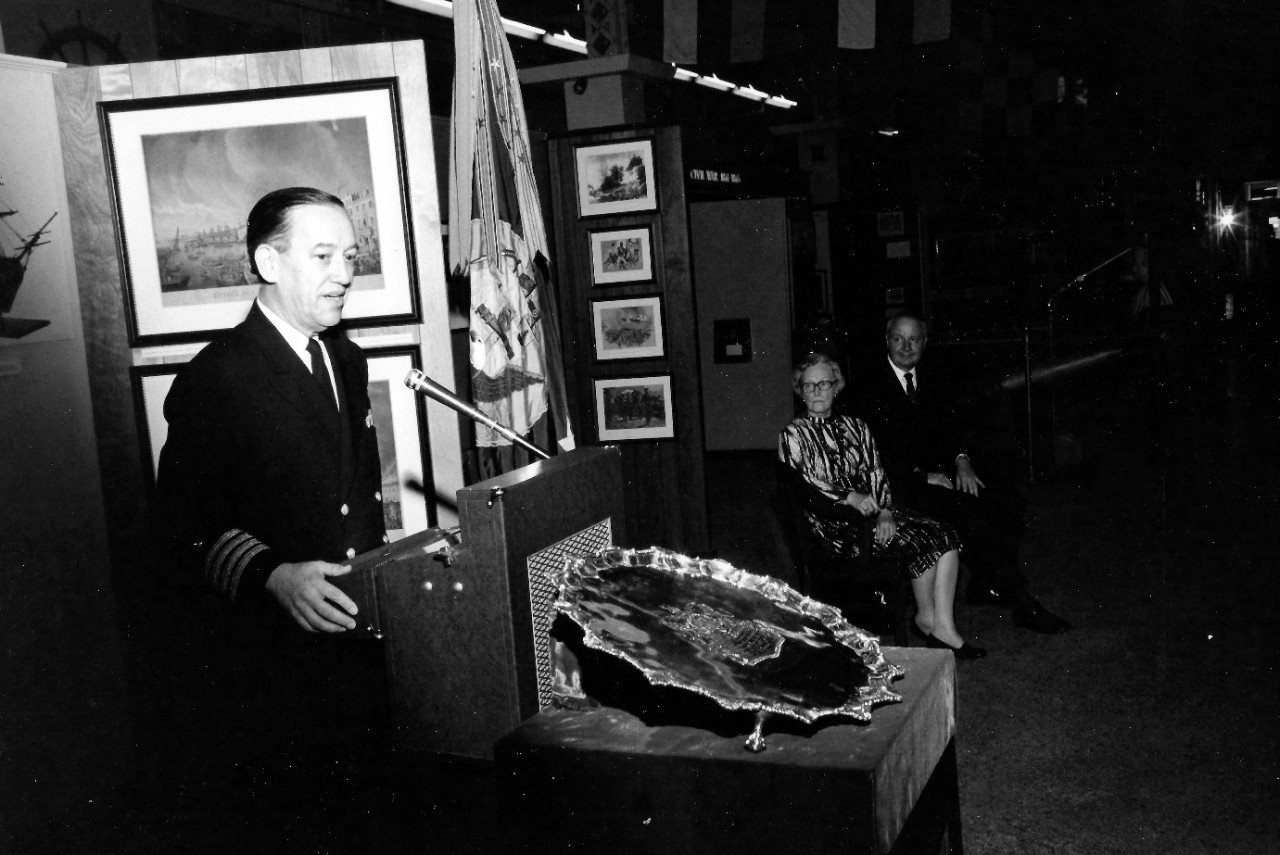 NMUSN-139: Presentation of HMS Intrepid Silver Tray, April 1975. Shown: Navy Memorial Museum Director Captain Roger Pineau, USNR, gives remarks while Mrs. Edward Murrow and Secretary of the Navy J. William Middendorf look on at the Navy Memorial ...