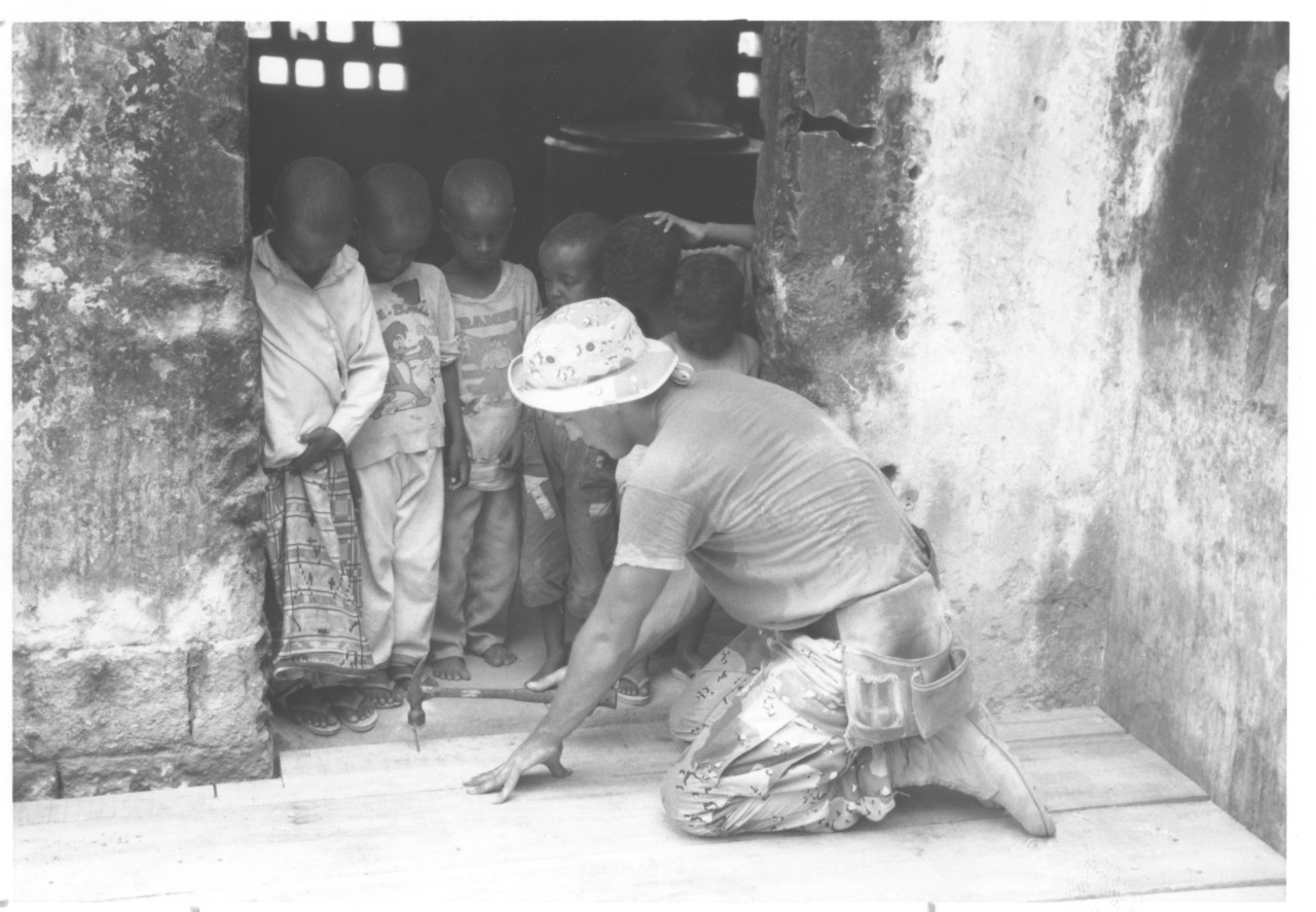 Seabee with NMCB-40 repairing an orphanage in Somalia as part of Operation Restore Hope as Somalian children look on, [January 1993].