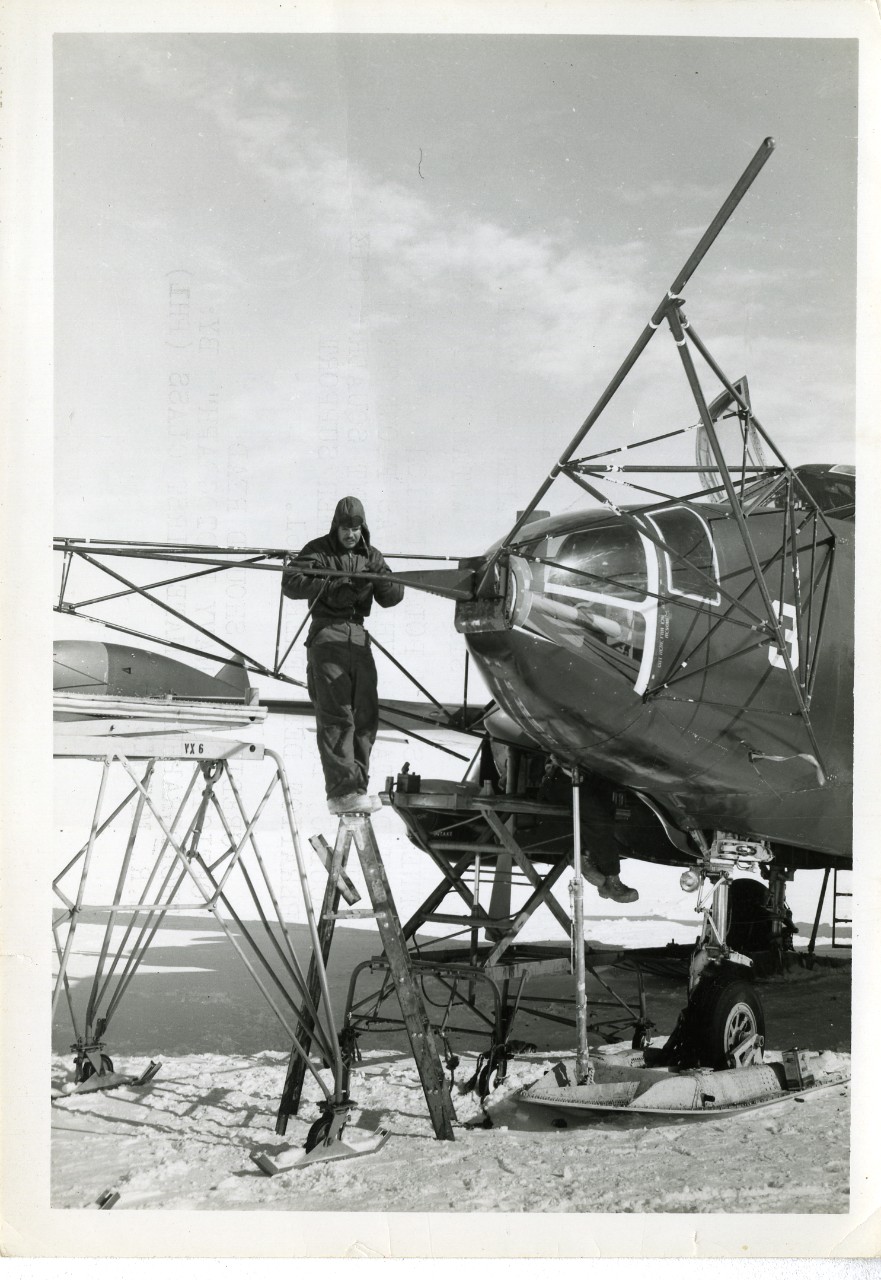 Black and white photograph of AM1 William W. Chastain from Carmi, Illinois tightening the nose mount bolts on the Air Retriever on P2V-7 Ski Aircraft Buno, 25 January 1961