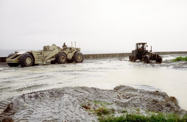 Seabees assigned to NMCB 4 are using a bulldozer and front loader to remove wet ash from Subic Bay and Cubi Point. 