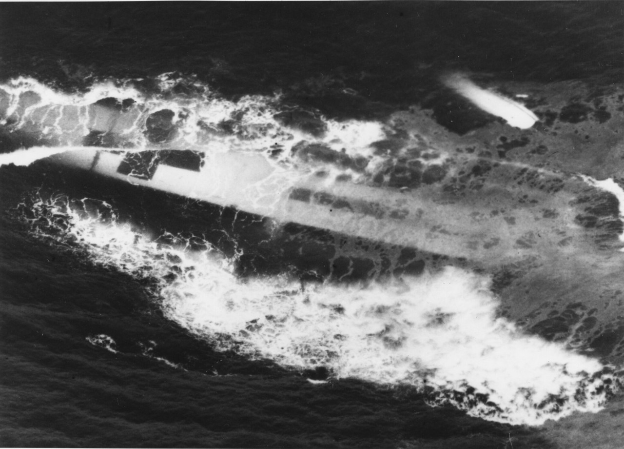 Aerial black-and-white photograph of sinking ship visible under the surface of the water. 