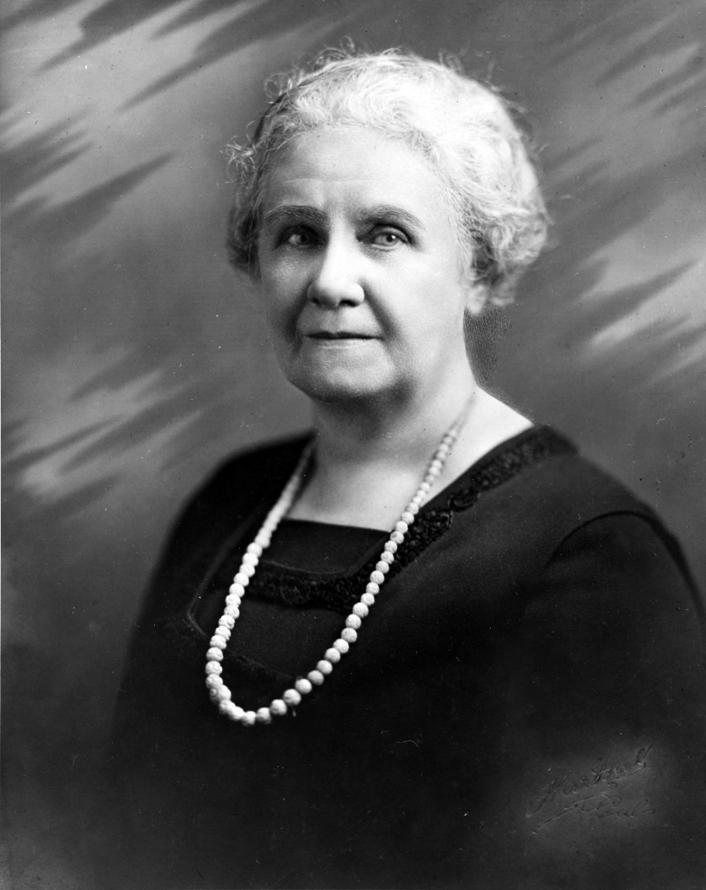 Portrait photo of Esther Hasson, dressed in a black dress with a white necklace