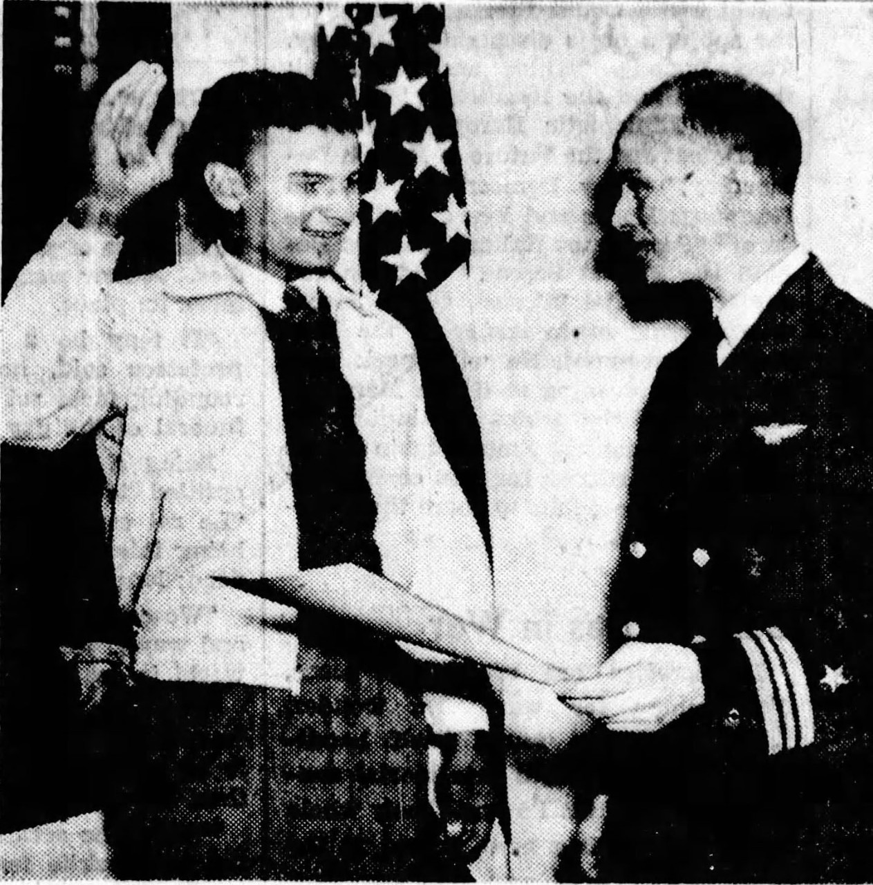 Man in civilian clothing raises his right hand while looking at a man in uniform.