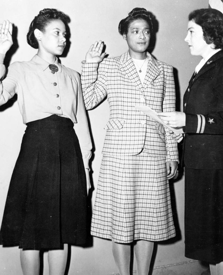 Two women raising their right hands facing a uniformed woman holding a piece of paper.