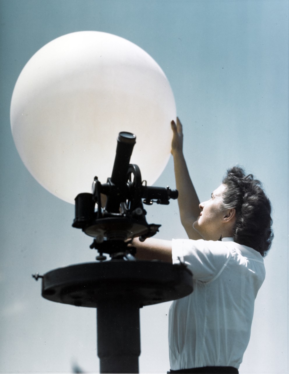 A woman holds a white weather balloon above a black platform.