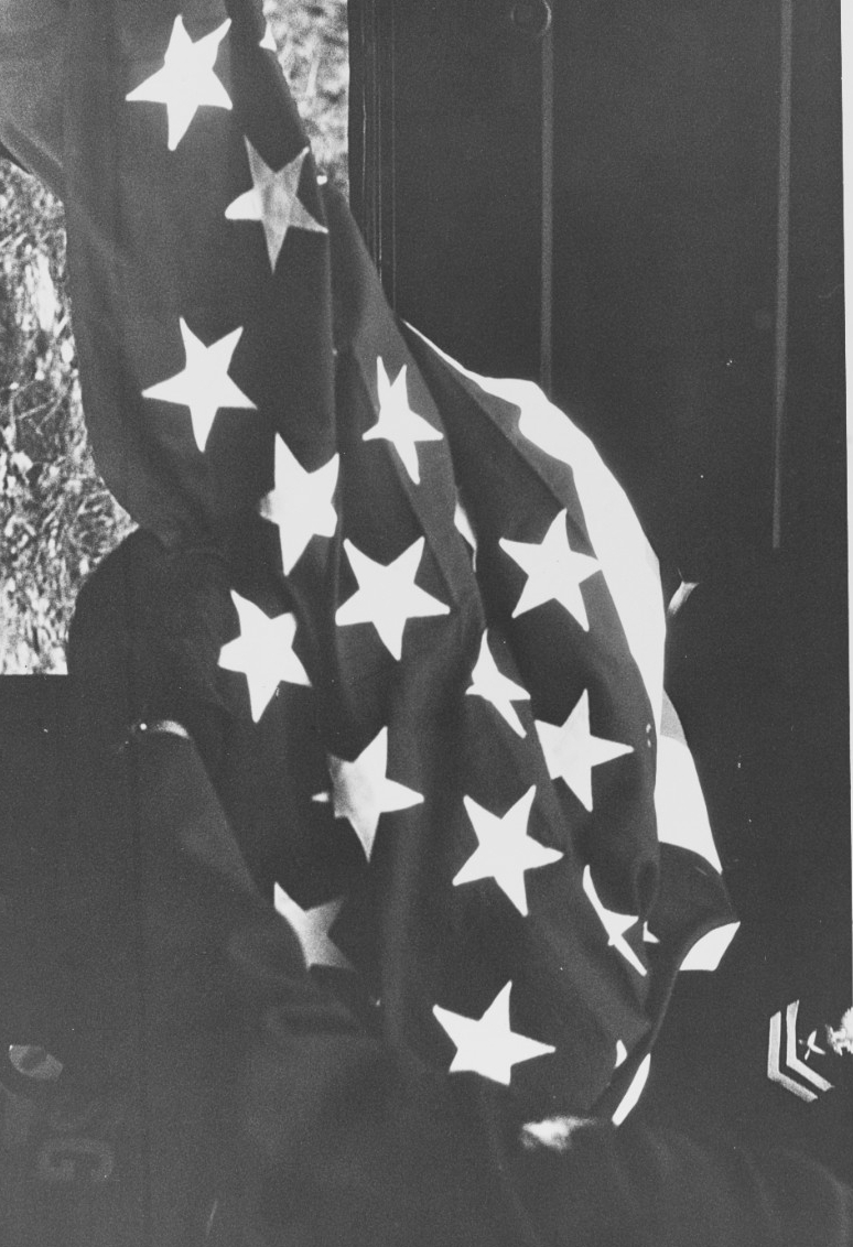 A Navy Yeoman Second Class holds a U.S. flag, to be used to drape the coffin of Seaman Duane Hodges. Click image to download.