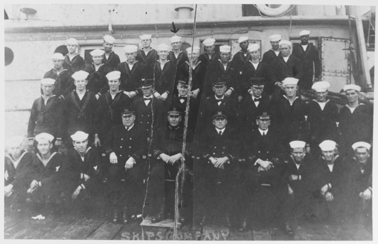 black and white photo of men standing in 4 rows on deck in front of ship in uniform