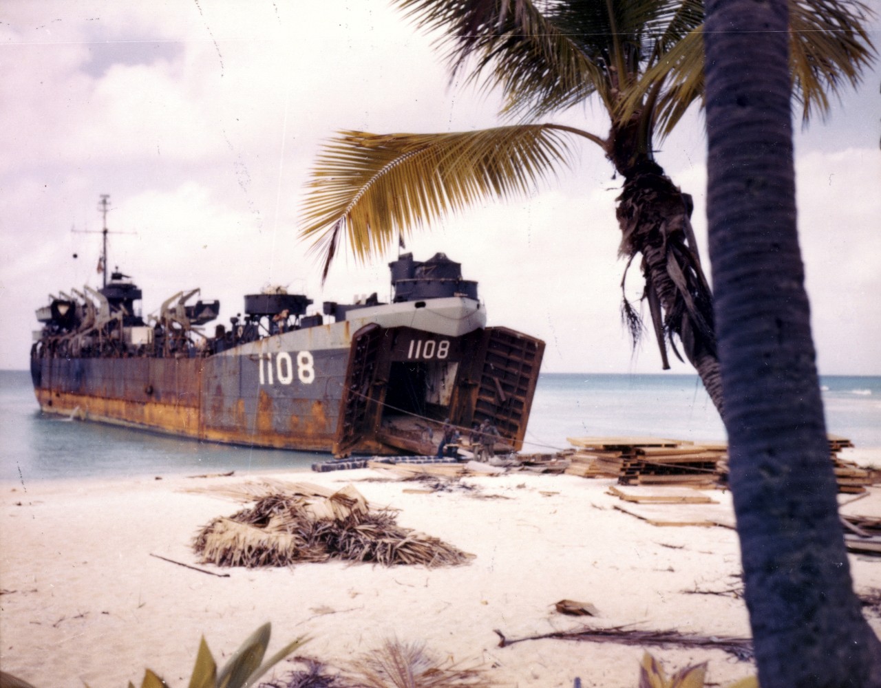 LST vessel arrives on a beach, palm tree in foreground