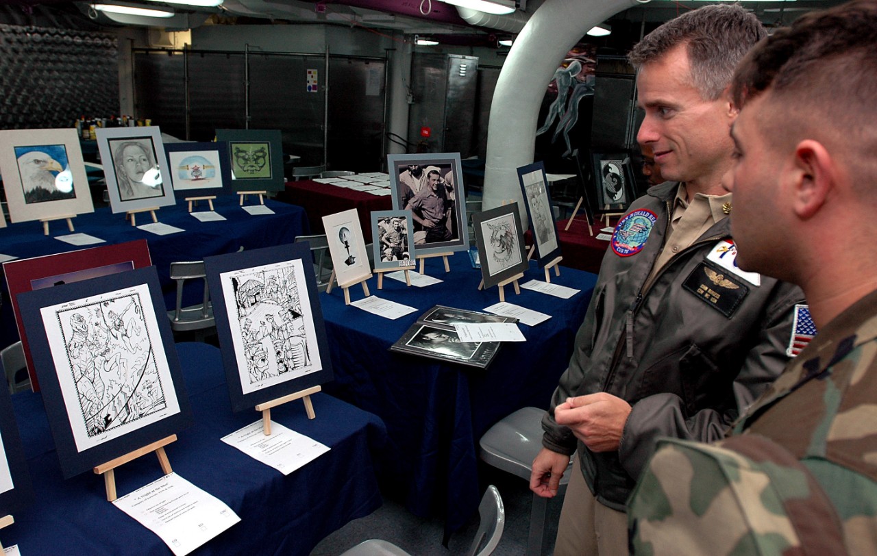Storekeeper 2nd Class David Hyatt, right, provides the USS Ronald Reagan (CVN 76) Senior Medical Officer, Cmdr. John Burgess, with some insight into his comic book style artwork during the ship's firs "Metropolitan Art Center Juried Art Show and ...