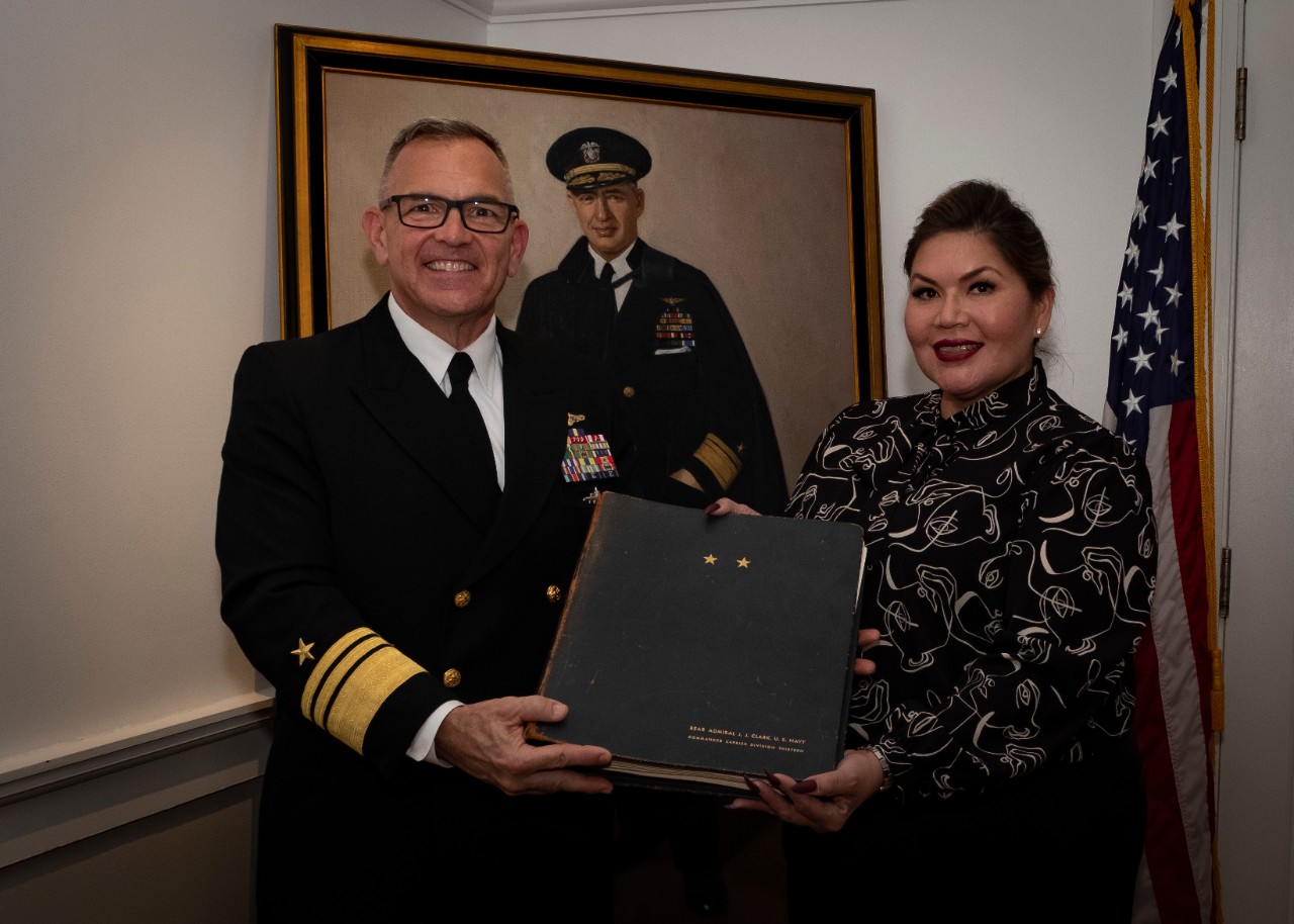Deputy Chief of Naval Operations for Information Warfare, Vice Adm. Jeffrey Trussler, presents a cruise book owned by the late Adm. Joseph Clark, a member of the Cherokee Nation and the first Native-American U.S. Naval Academy graduate, to Kimber...