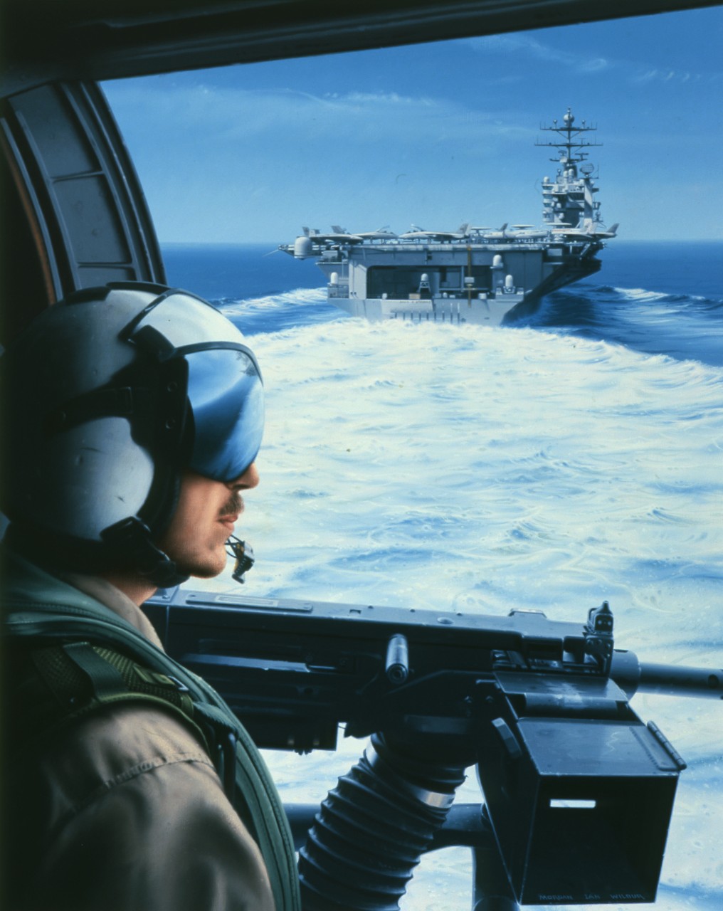 A crewman looks out the hatch of a helicopter, he is looking at the stern of an aircraft carrier