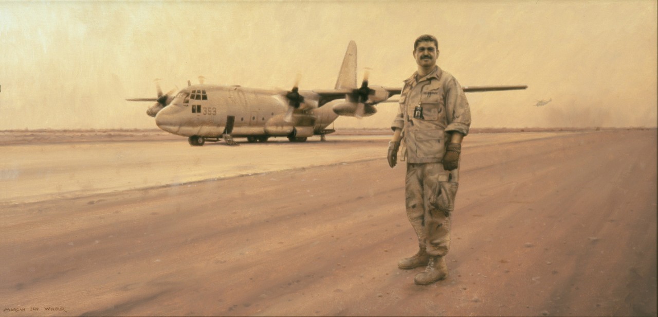 A man in uniform stands on the runway, in the background is a C-130 airplane. A sand storm is causing an orange light