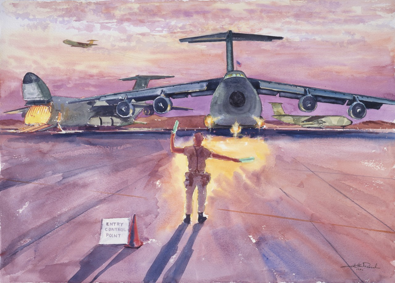 A marine directs a cargo plane at sunset, in the background are two other planes - the one on the left side has its nose open for unloading