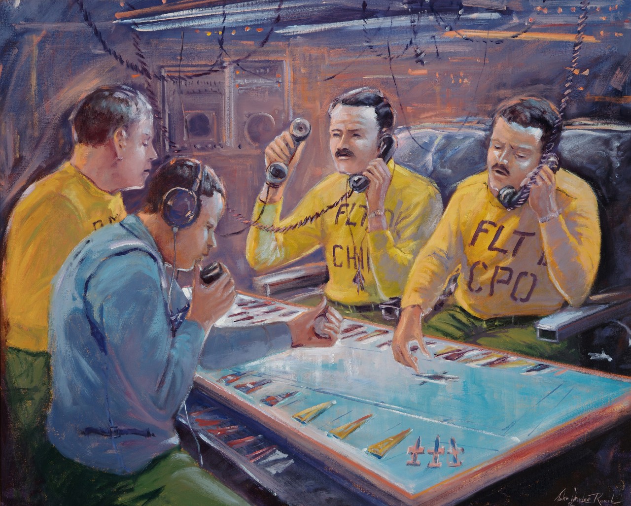 Four men at a table; three are wearing yellow shirts, two are talking into phones, one man wearing a blue shirt as a headset.