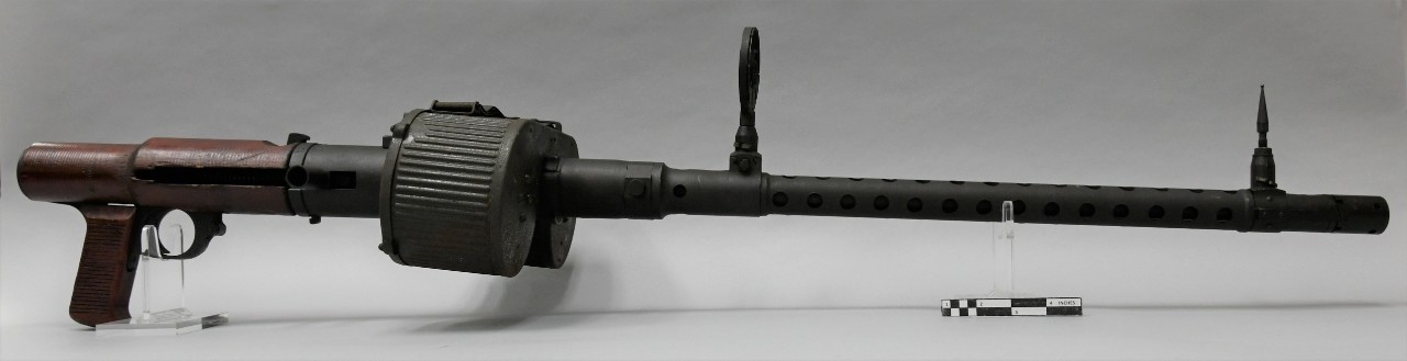 Right side of a Japanese Type 98/Type 1 aircraft machine gun. The gun has a long metal tubular barrel. The rear of the receiver and pisotl grip have brown wood covers. A detachable 75-round saddle magazine is attached to the top of teh receiver.