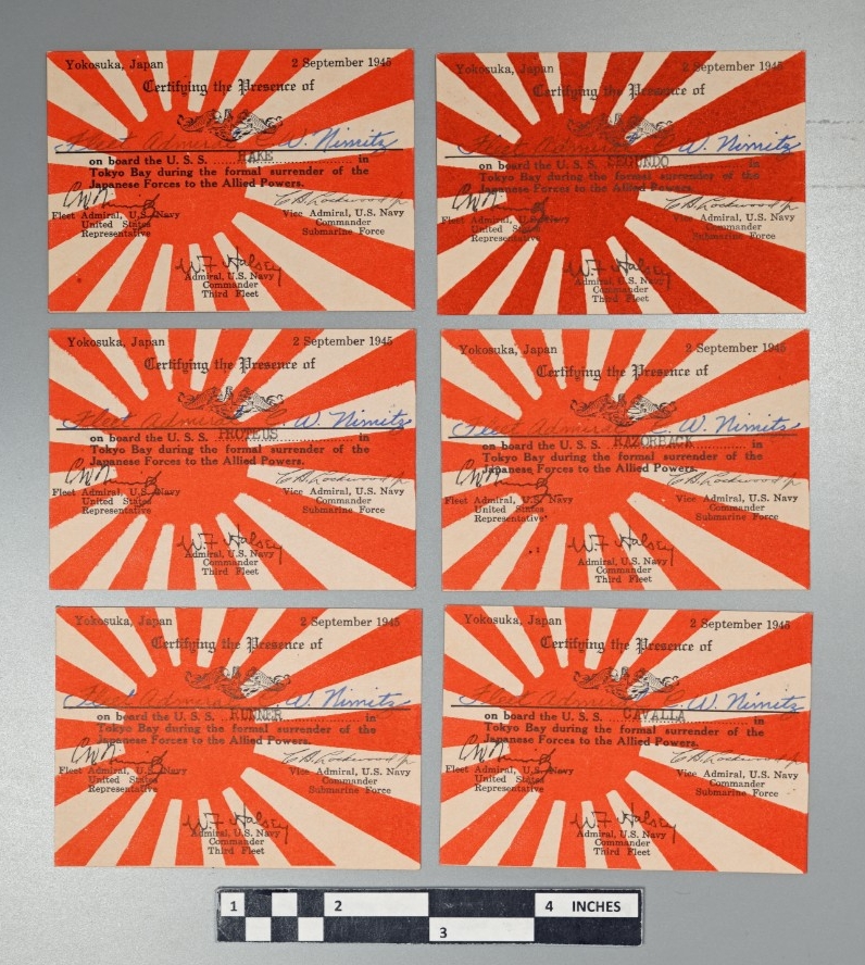 A group of seven small, 2.55” x 3.54” rectangular cards of white cardstock. The background of the obverse has a representation of the Imperial Japanese Navy ensign printed in red consisting of a disc offset to the left with rays radiating out fro...