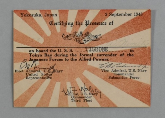 A small, 2.55” x 3.54” rectangular card of white cardstock. The background of the obverse has a representation of the Imperial Japanese Navy ensign printed in red consisting of a disc offset to the left with rays radiating out from the disc. Over...