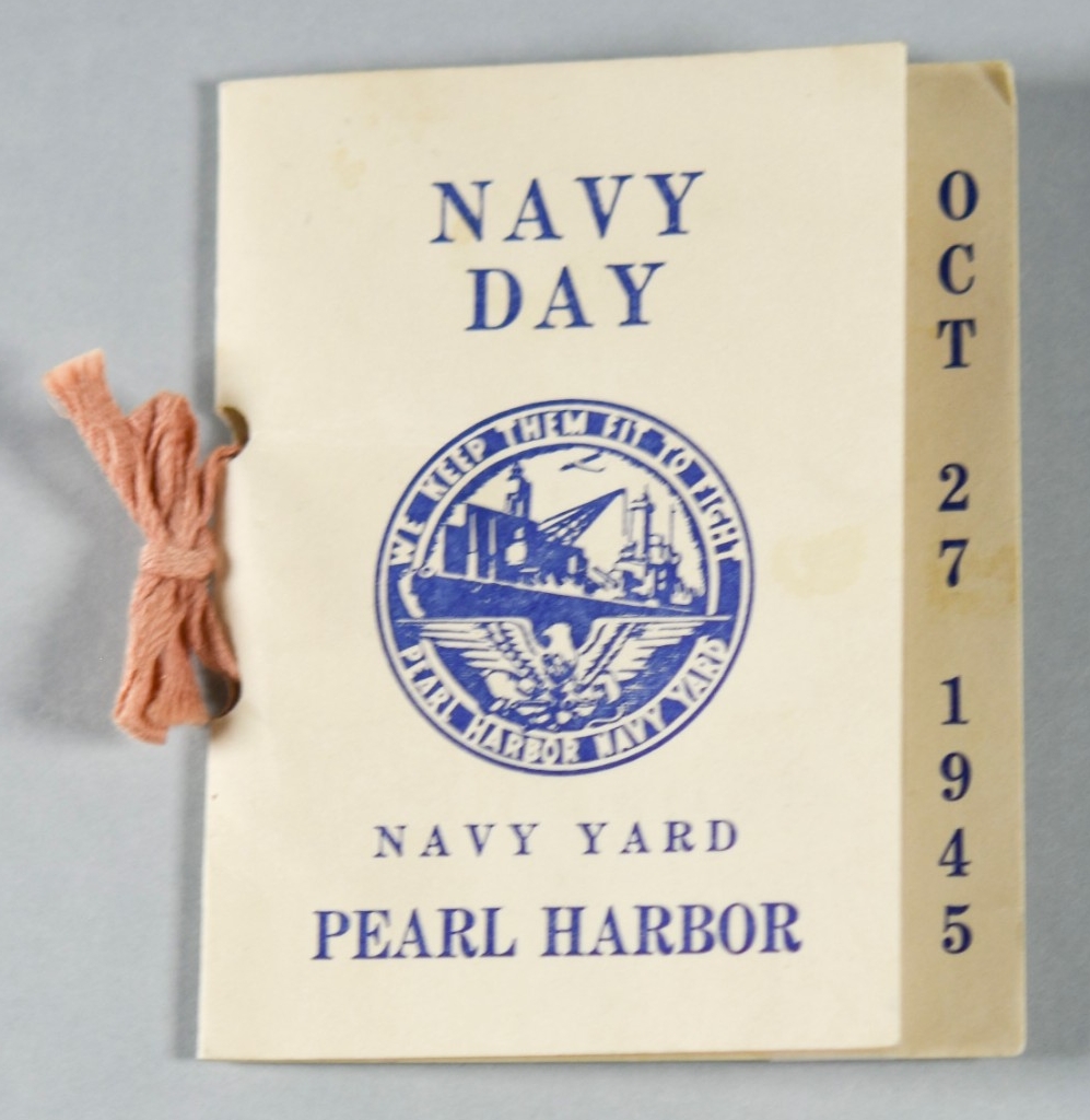 A 3.5” x 4” rectangle of white cardstock folded over to form a small souvenir card. The obverse reads: NAVY / DAY / NAVY YARD / PEARL HARBOR. A circular logo at the center of the obverse has lettering around the rim which reads: WE KEEP THEM FIT ...