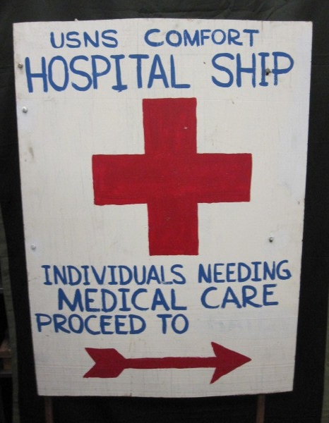 White wooden sign with blue lettering and a red cross and arrow directing for medical care