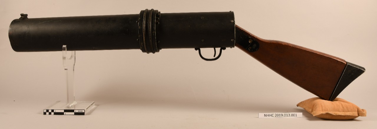 Reverse view of blinker tube/signal light gun. Black metal tube, trigger on underside, wood gun stock.    