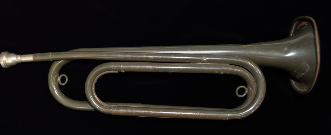 One military-issued service bugle. Brass or copper alloy body painted gray. The body has a double twist shape and a white metal mouthpiece. The bell is stamped “BUGLECRAFT INC./L.I. City, N.Y./U.S.”