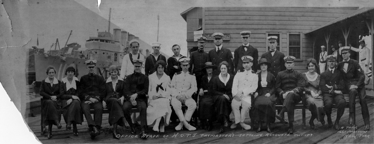 Single oversized image of the office staff and paymasters of the Naval Overseas Transportation Service (N.O.T.S), New York, July, 1919. Photograph taken by H. Tarr. There is damage to the lower left hand side of the photo.  