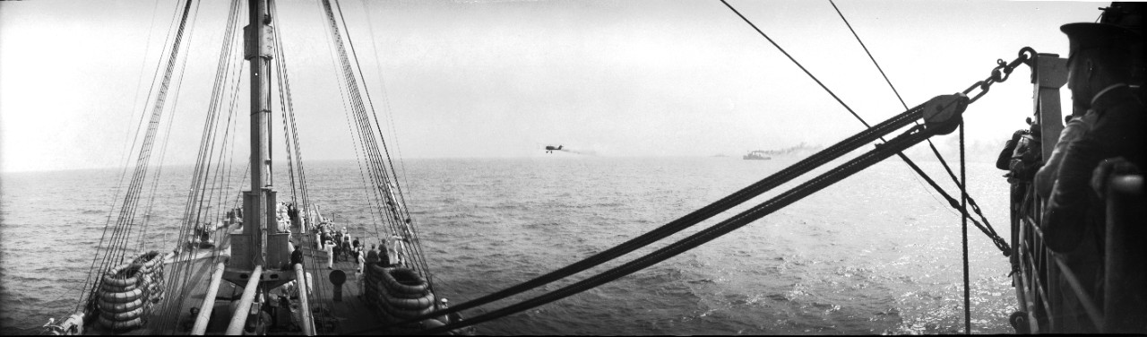 A DH-4 bomber flies low, past the starboard side of USS Henderson (AP-1). Henderson hosted press reporters, military officers, and foreign observers as they observed the 1921 Army-Navy bombing experiments off the Virginia capes. 