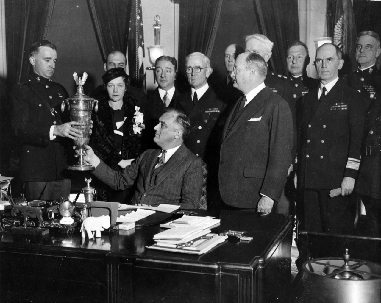 President Franklin D. Roosevelt presents the Herbert Schiff Trophy for naval aviation safety to a Marine aviator, at a ceremony in the White House. At center, standing, is Chief of Naval Operations Admiral William H. Standley. Also seen are Rear Admiral Ernest J. King (standing, center rear) and Rear Admiral William Leahy (at right).