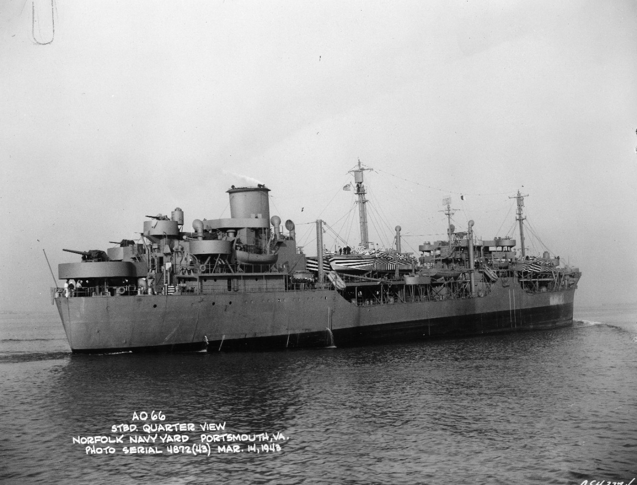 Starboard bow view of USS Atascosa (AO-66) underway in light load condition with camouflaged PT boats as deck cargo fore and aft off the Norfolk Navy Yard, Portsmouth, VA, on 14 March 1943. She was the former S.S. Esso Columbia. Note the lines at her bow. She seems to be streaming paravanes.