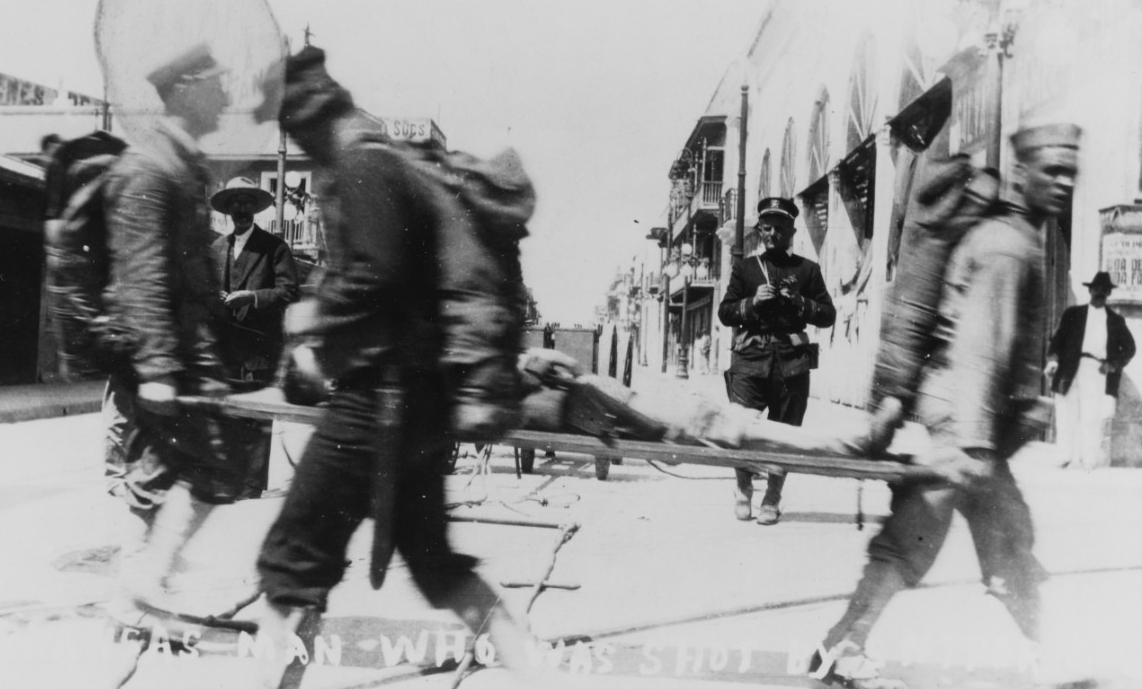 A chief petty officer and a sailor carry a wounded Arkansas crewman hit by a sniper at Veracruz, 22 April 1914. The stretcher bearer party wear dyed “whites,” while the other men wear their blue uniforms. (Naval History and Heritage Command Photo...
