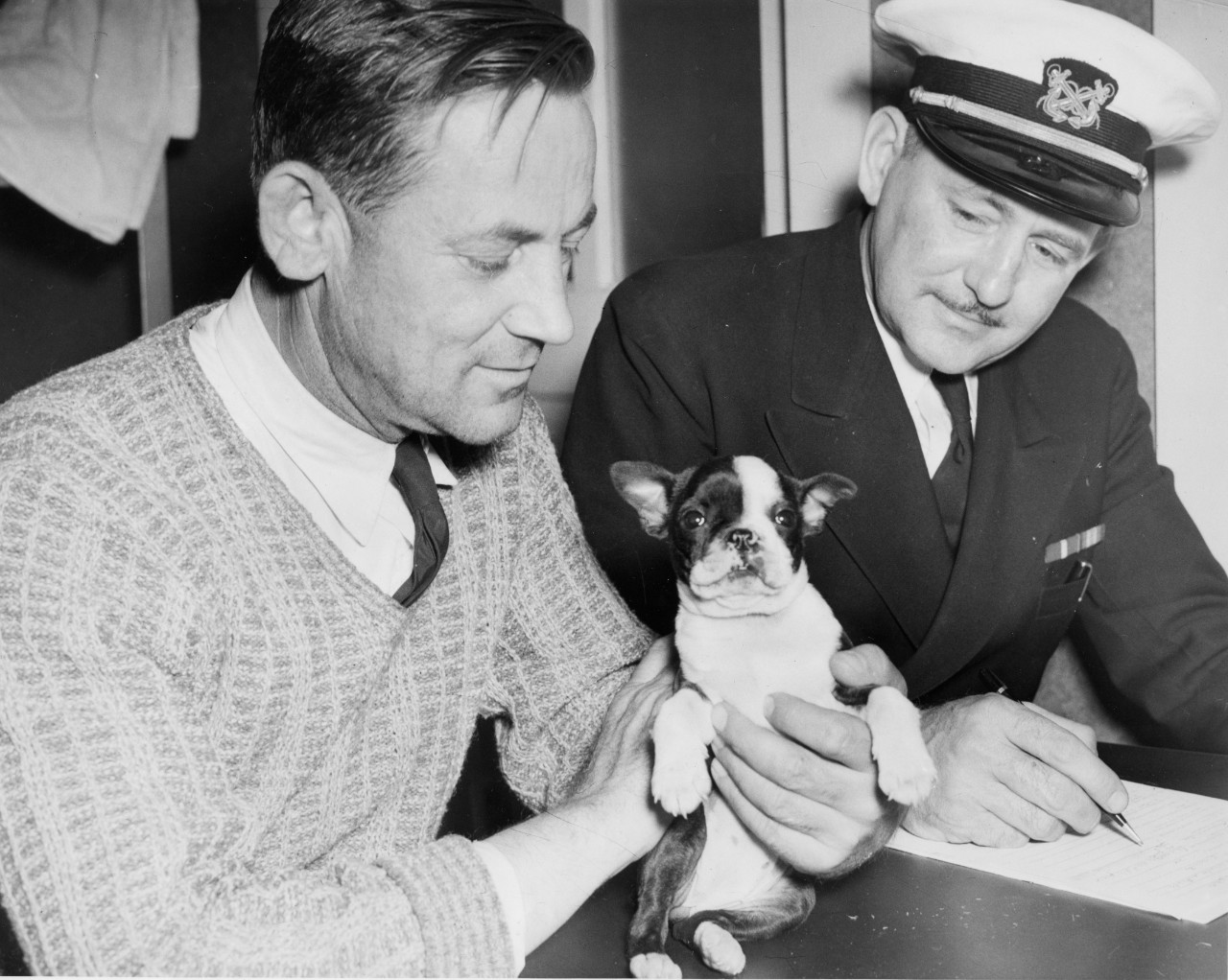 Capt. George Fisk, Empire Thrush’s master, holds “Elizabeth,” his 5-week old Boston Bulldog, during the debriefing of his ship’s crew. (U.S. Navy Photograph 80-CF-105-4A-1, National Archives and Records Administration, Still Pictures Branch, Coll...