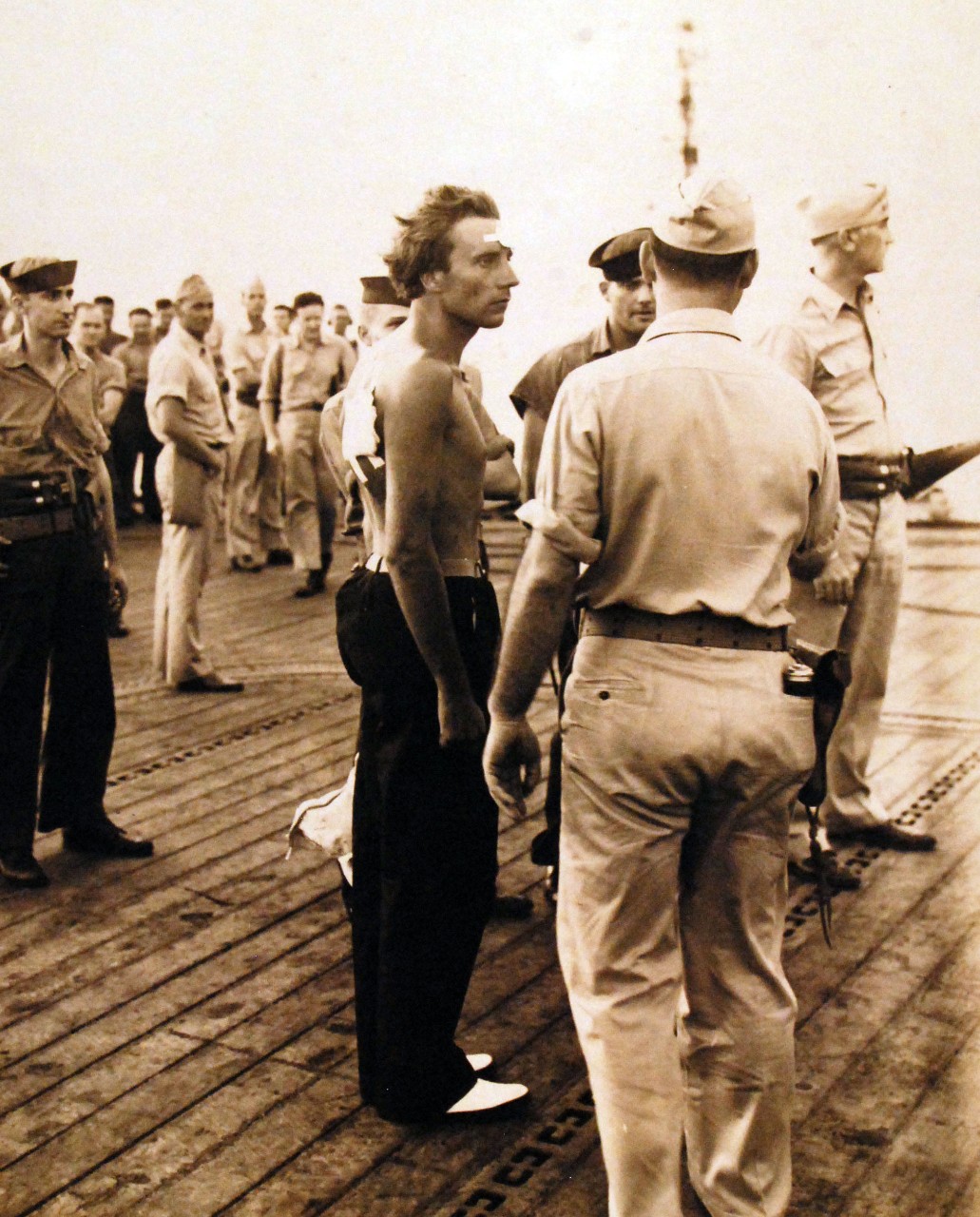 80-G-77199: Air attacks on German U-boats, WWII. The German captain of U-185 and U-604 survivors onboard USS Core (CVE-13), August 24, 1943. They are being directed by the Master-At-Arms. Incident #4082. 