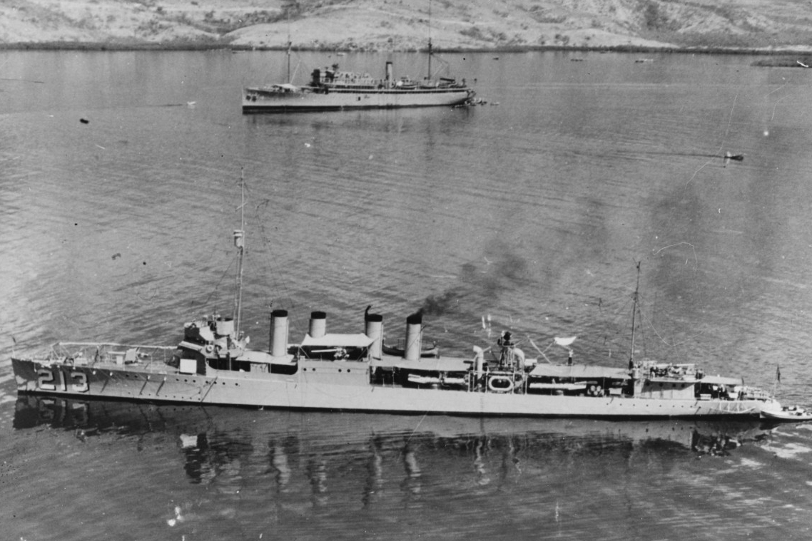 Barker puts in to Gonaives, Haiti, March 1928. She has steam up in a single boiler, a seaman hangs wash on one of the lines just aft of amidships, and a boat is tethered to her stern. Other vessels come and go in the busy harbor as the fleet carr...