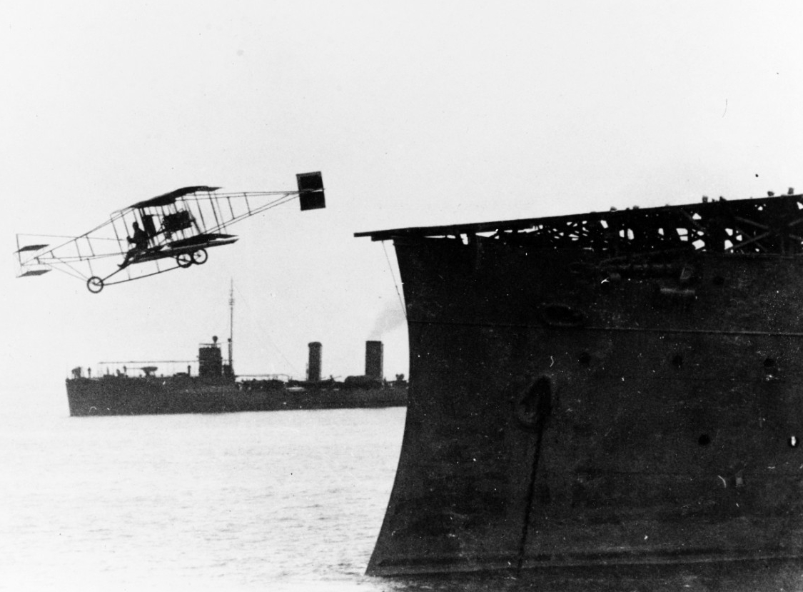 Ely flies his plane off the deck of Birmingham, 14 November 1910. Roe (Destroyer No. 24) is among the ships that stand by during the historic event and is visible in the background. (Naval History and Heritage Command Photograph NH 76511)