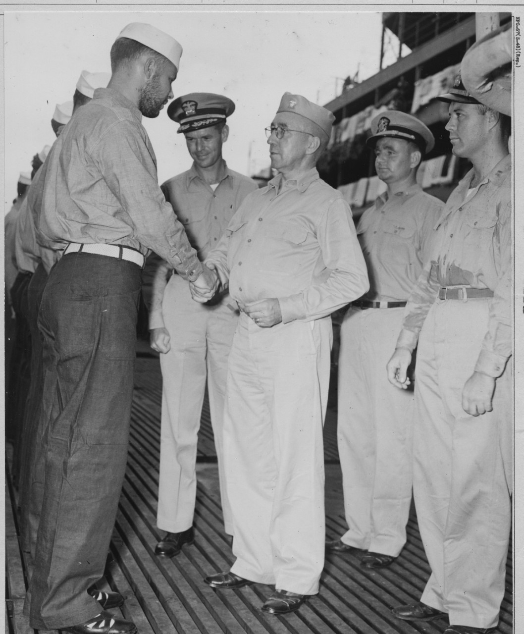 While Cmdr. John F. Davidson looks on approvingly, Rear Adm. Fife exchanges pleasantries with a bearded member of Blackfish’s crew on the occasion of the men being awarded their Submarine Combat Insignias, 23 December 1943. Note bedding airing on...