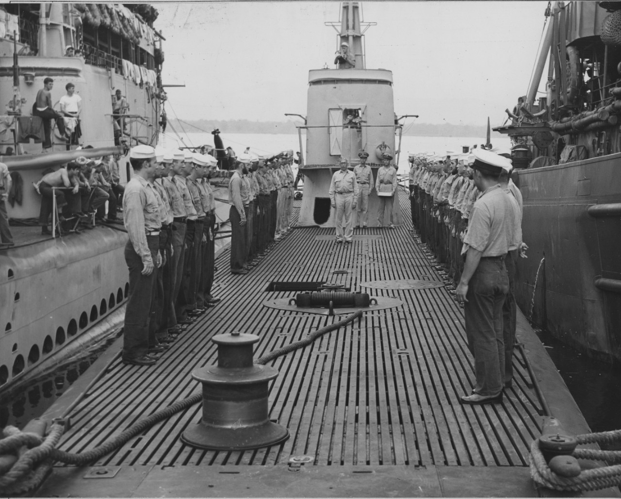 Rear Adm. James Fife addresses Blackfish’s crew, standing at attention, as he provided them with their Submarine Combat Insignias, 23 December 1943. Note how the sailors on board the boat moored alongside (L) display a more casual onlooker’s stan...