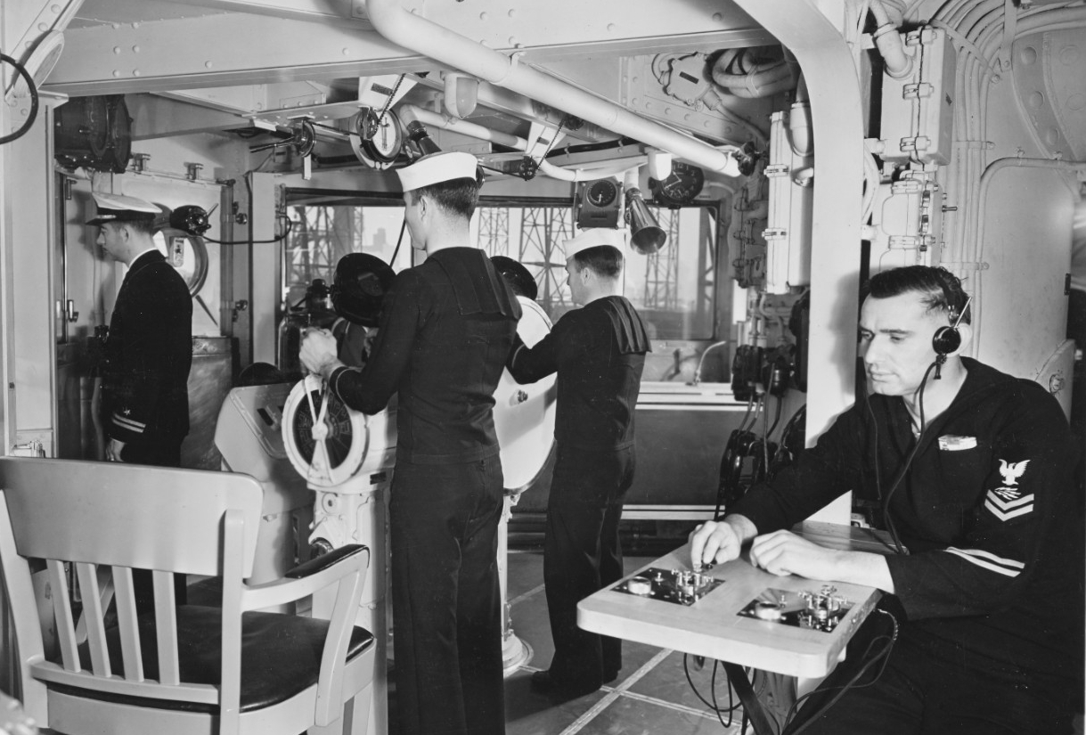 A scene of Brooklyn’s pilothouse, looking to starboard, as the ship completes her construction at the New York Navy Yard, 18 January 1938. Note the men at the helm and engine order telegraph (left), and the radioman at the communications table (r...