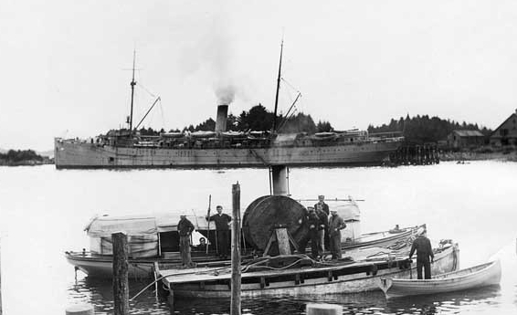 Boats from Buffalo preparing to lay a communications cable at Sitka, Alaska, in fall 1914, during the Alaskan Radio Expedition. A steam launch from the ship is alongside an improvised pontoon carrying the cable reel. (Naval History and Heritage C...