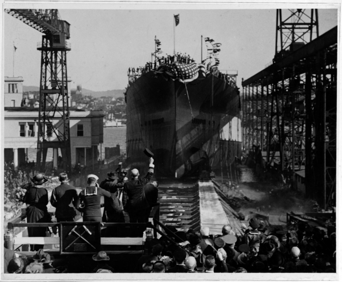 California slides down the way during her launching ceremony at the Mare Island Navy Yard on 20 November 1919. The group standing on the christening stand to the lower left of the photograph includes Mrs. Barbara S. Zane, daughter of the state’s Governor William D. Stephens and the ship’s sponsor (on the left), a Navy captain lifting his hat to the battleship, a motion picture cameraman, and a bugler. (Naval History and Heritage Command Photograph NH 55016)