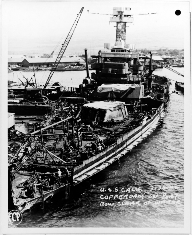 Workmen repair the ship after she is raised and moored at Pearl Harbor, 30 March 1942. Note the cofferdam installed along her port bow and the forward turrets with their guns removed. (Courtesy of Vice Adm. Homer N. Wallin, U.S. Navy Photograph NH 55036, Photographic Section, Naval History and Heritage Command)