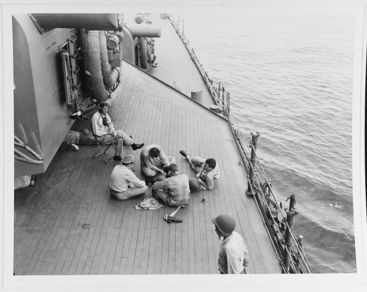 Men rest on Chicago’s deck beside 8-inch turret No. II, 9 August 1942. The view looks forward on the starboard side, as the ship appears to be underway. Note the lookout in the chair wearing the headphones, the .45 caliber M1911 pistol in the hol...