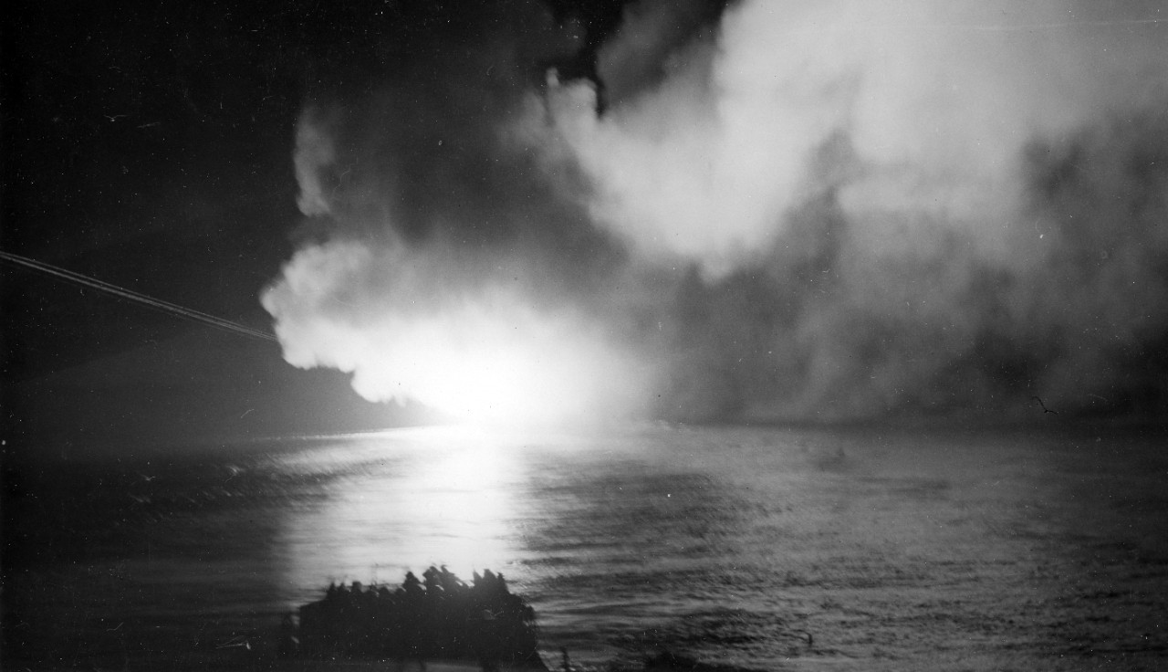 Completely enveloped with smoke from her own gunfire, Cleveland bombards targets on northern Bougainville Island on 24 December 1943 (as seen from her sister ship Columbia (CL-56)). Note the bright streaks on the left tracing the trajectory of a ...