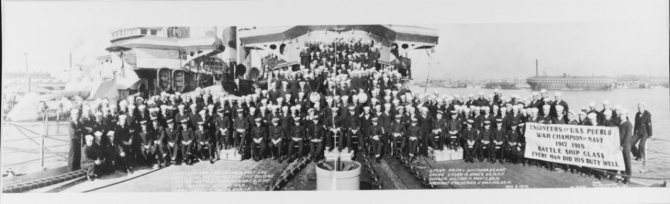 A panoramic photograph of Pueblo’s Engineering Crewmen, taken on her forecastle at Norfolk, Va., 3 December 1918. Note the banner proclaiming: “Engineers of U.S.S. Pueblo...War Champion of Navy...1917–1918...Battle Ship Class...Every man did his job well”. The ship alongside, at left, is probably Huron (Armored Cruiser No. 9). She is still painted in pattern camouflage. Receiving ship Richmond is in the right distance. Photographed by the G.L. Hall Optical Co., of Norfolk.
