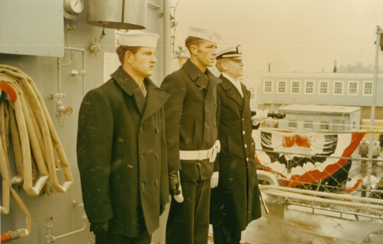 As a tribute to both the ship and its namesake, Cook's first watch consisted of (L to R) Seaman Thomas M. Cook (Messenger), Commissaryman First Class Clarence J. Cook (Petty Officer of the Watch), and Ensign Roger D. Cook (Quarterdeck Watch Offic...