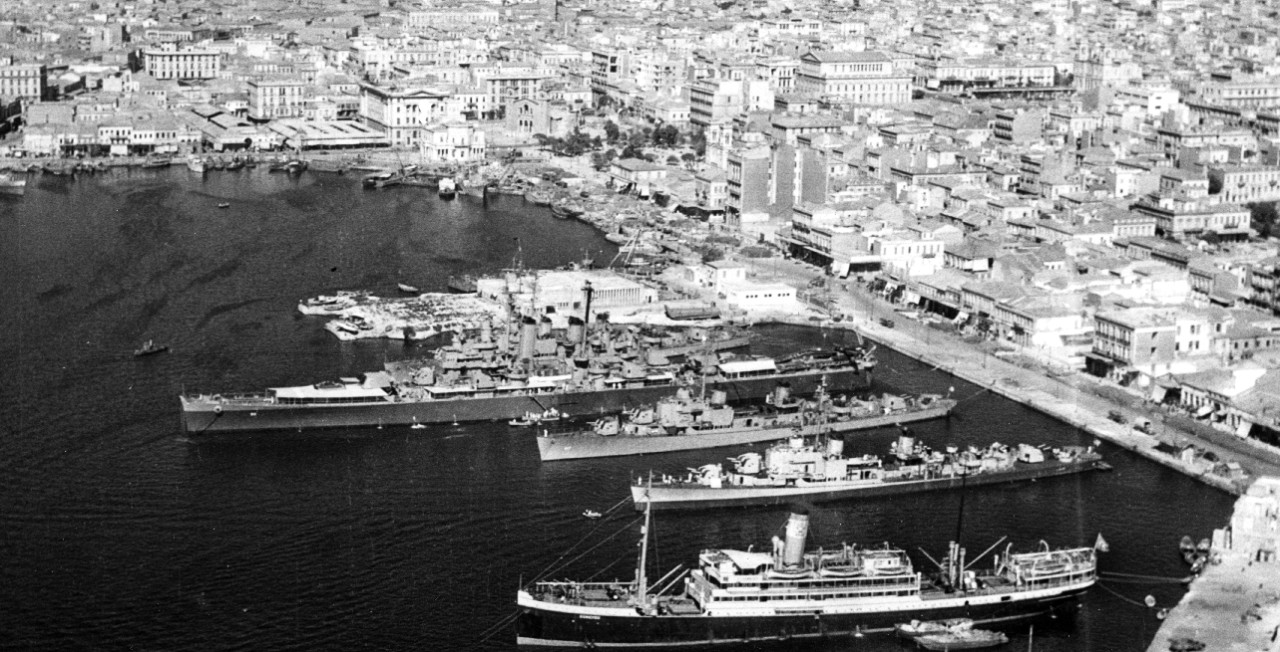 Little Rock, Cone, Corry, and New (DD-818) lay at Piraeus, the seaport for Athens, 6 September 1946. The ships are Mediterranean-moored (i.e., stern to shore). Note the differing paint schemes on the two destroyers moored in the foreground, refle...