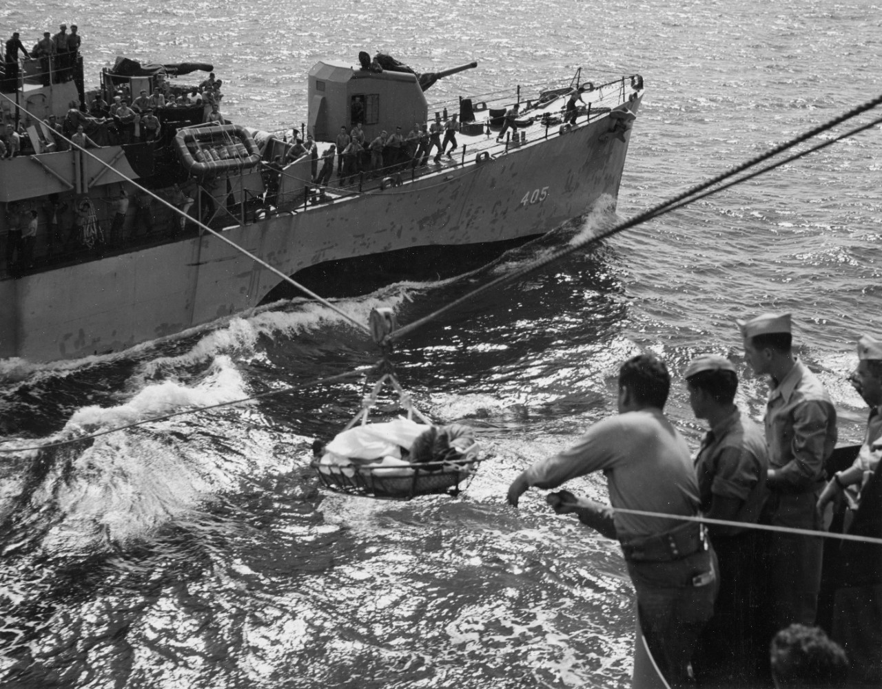Dennis (background) transfers S1c Harold J. Scribner, V-6 SV, USNR, to Sangamon (CVE-26) for emergency medical treatment on 21 September 1944. Note the men on Dennis’ main deck handling the required lines, as well as shipmates topside watching fr...